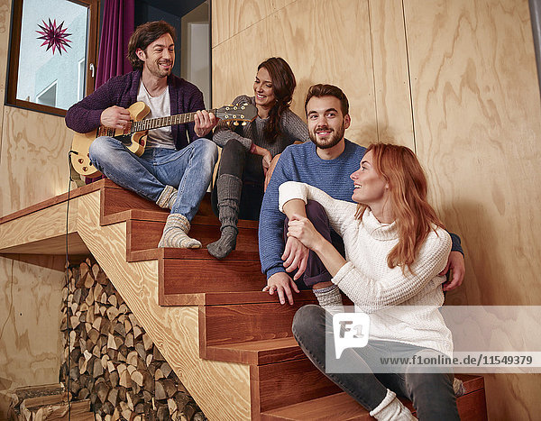 Freunde sitzen auf einer Holztreppe und spielen Gitarre.