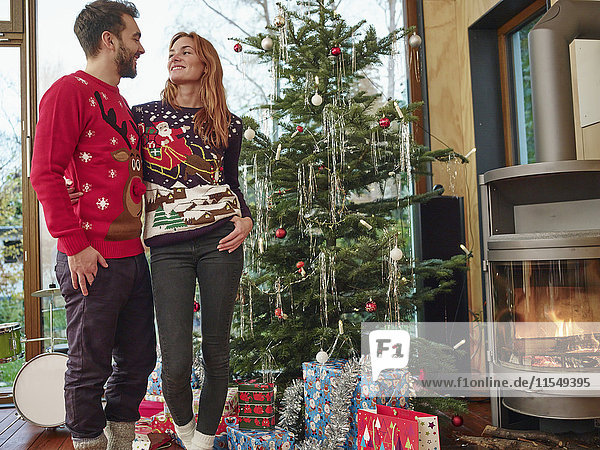 Glückliches Paar vor dem Weihnachtsbaum mit Weihnachtspullover
