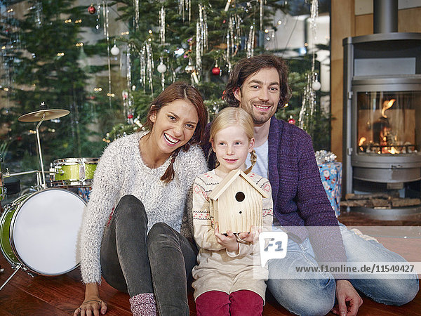 Eltern sitzend mit Tochter vor dem Weihnachtsbaum  lächelnd