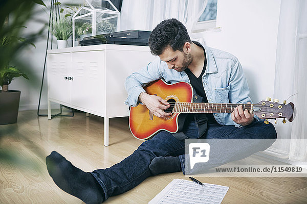 Junger Mann sitzt auf dem Boden und spielt Gitarre.