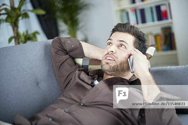 Young man talking on smartphone lying on couch