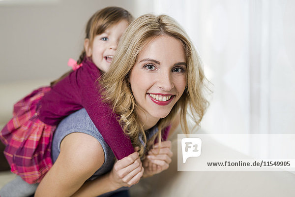 Porträt einer lächelnden Frau  die mit ihrer kleinen Tochter auf der Couch im Wohnzimmer spielt.