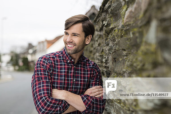 Porträt eines lächelnden Mannes mit kariertem Hemd an der Steinmauer lehnend