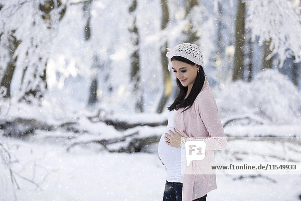 Lächelnde schwangere Frau im Freien bei Schneefall