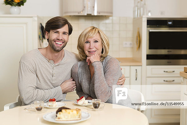 Porträt einer glücklichen Mutter und eines erwachsenen Sohnes,  die in der Küche sitzen.