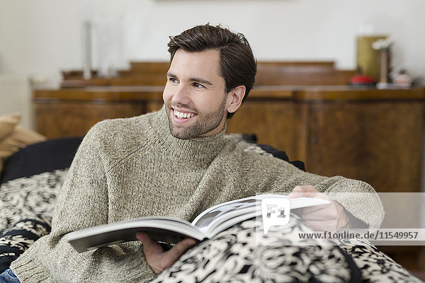 Porträt eines lächelnden Mannes auf der Couch mit Buch