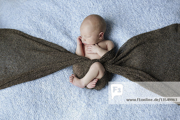 Nacktes Neugeborenes mit einem auf einer Decke liegenden Schal bedeckt