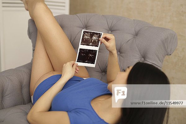 Pregnant woman in armchair looking at ultrasound scans