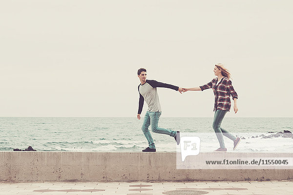 Ein junges Paar  das Hand in Hand am Meer geht.