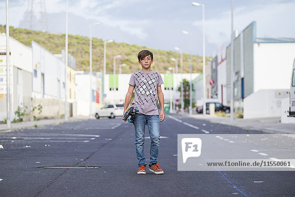 Spanien  Teneriffa  Portrait eines Jungen  der mit seinem Skateboard auf einer Straße steht.