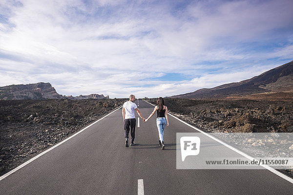 Spain  Tenerife  back view of couple walking hand in hand on empty road at Teide National Park