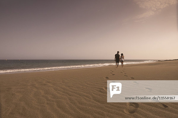 Spanien  Teneriffa  Rückansicht eines verliebten jungen Paares beim Spaziergang am Sandstrand