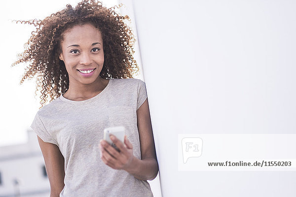 Spain  Tenerife  portrait of smiling woman with afro holding smartphone