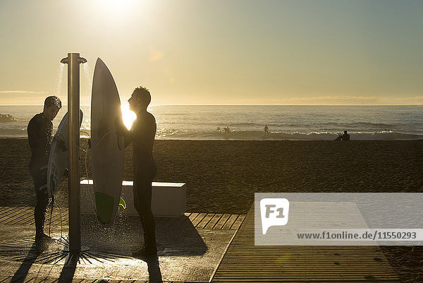 Zwei Surfer bei Sonnenaufgang am Strand  Dusche