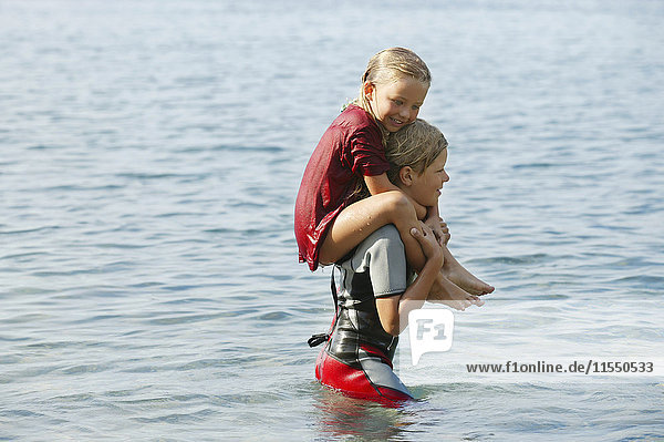 Spanien  Mallorca  Junge mit kleiner Schwester auf den Schultern im Meer
