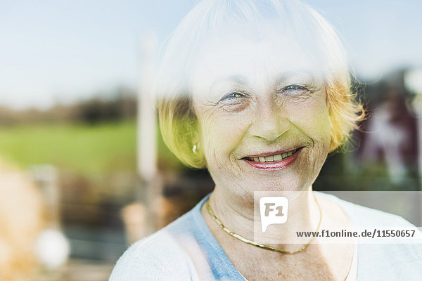 Porträt der lächelnden Seniorin hinter der Fensterscheibe