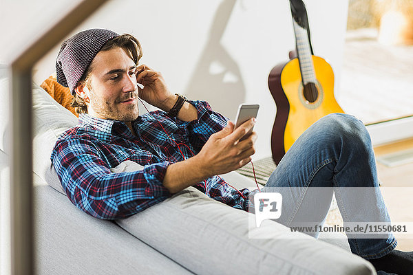 Portrait of young man sitting on the couch hearing music with earphones and smartphone