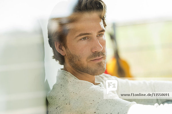 Portrait of pensive young man looking through windowpane