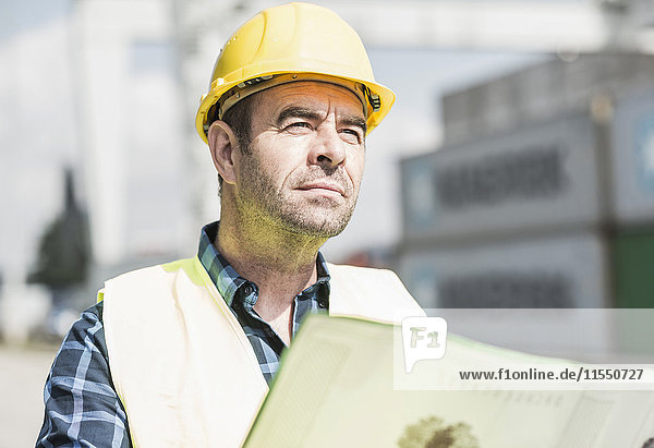 Man wearing hard hat holding document at container port