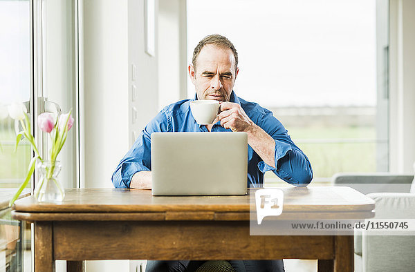 Geschäftsmann zu Hause mit Laptop am Holztisch