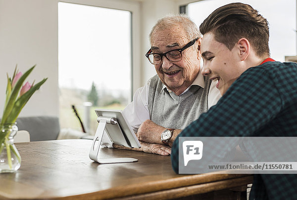 Glücklicher älterer Mann und sein Enkel schauen auf Mini-Tablette