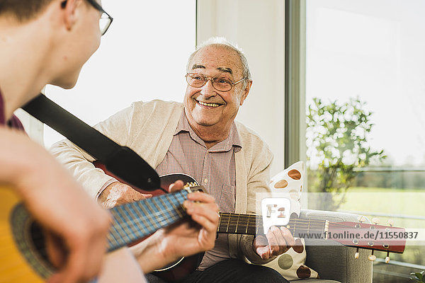 Porträt eines älteren Mannes  der mit seinem Enkel Gitarre spielt.