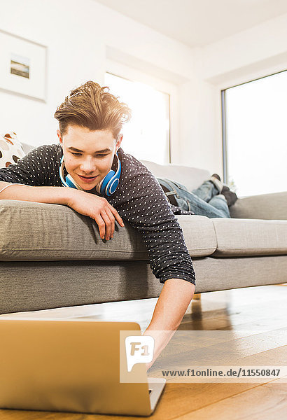 Junger Mann auf der Couch liegend mit Laptop