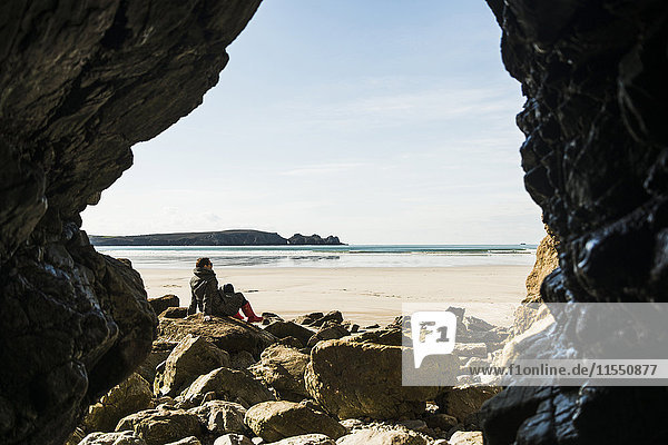 France  Bretagne  Finistere  Crozon peninsula  woman sitting on the beach as seen from rock cave