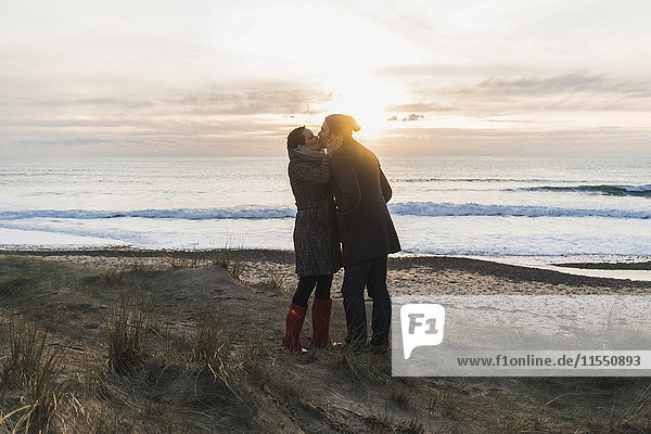 Frankreich  Bretagne  Finistere  Halbinsel Crozon  Paar  das sich bei Sonnenuntergang an der Küste küsst.