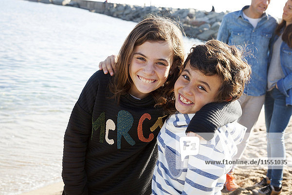 Spanien  Barcelona  Porträt der glücklichen Geschwister am Strand mit ihren Eltern im Hintergrund