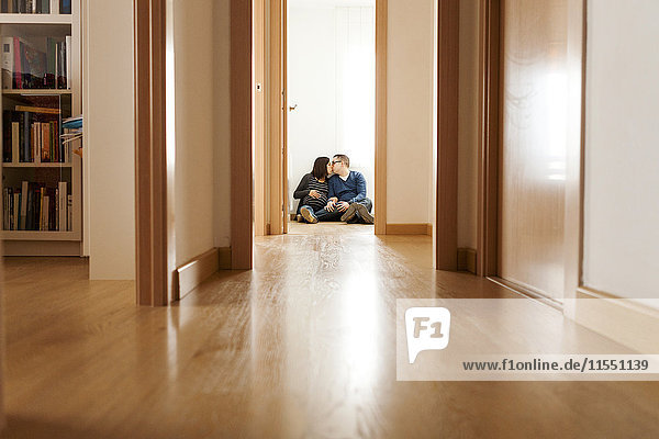 Erwartende Eltern  die auf dem Boden der Wohnung sitzen und sich küssen.