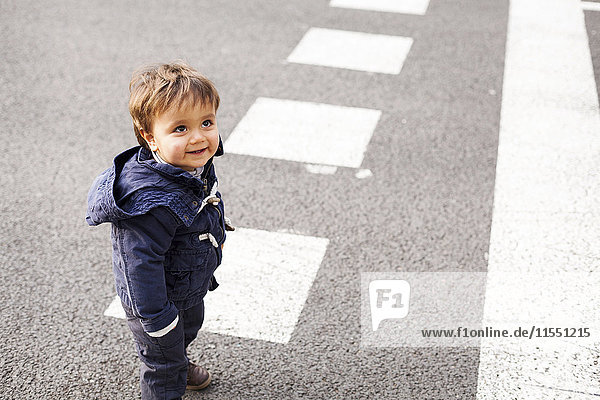 Porträt eines lächelnden kleinen Jungen  der auf einer Straße steht und nach oben schaut.