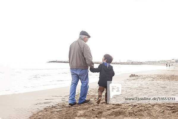 Großvater und Enkel gehen und reden am Strand.