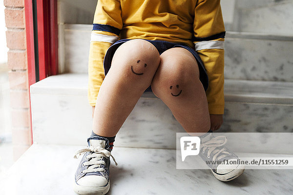 Boy sitting on stairs with smiley faces on his knees