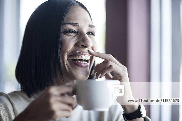 Portrait of laughing woman with milk moustache holding cup of coffee