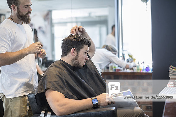 Young man at barber's shop discussing with hairdresser