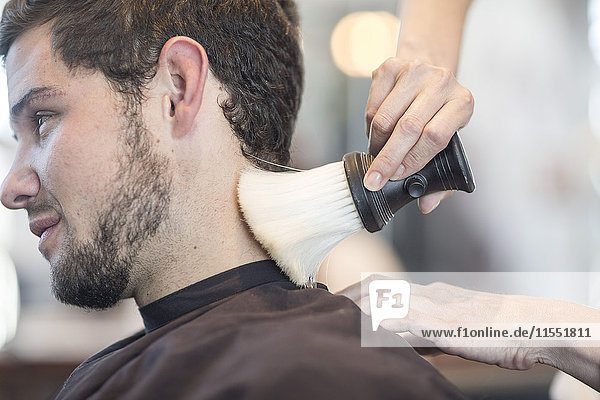 Junger Mann beim Friseur  der sich den Hals bürsten lässt.