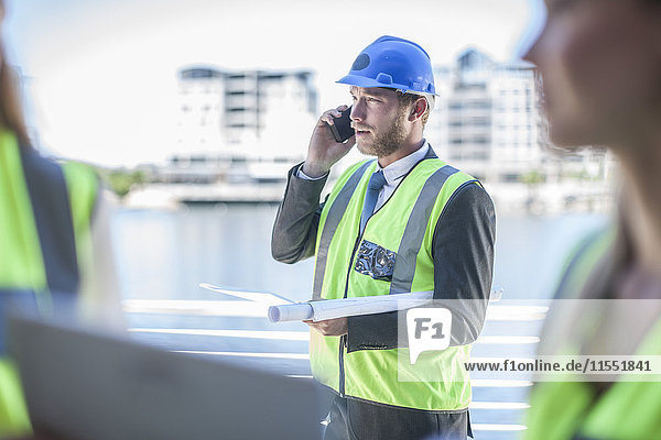 Ingenieur auf der Baustelle mit Blaupause  Telefongespräch
