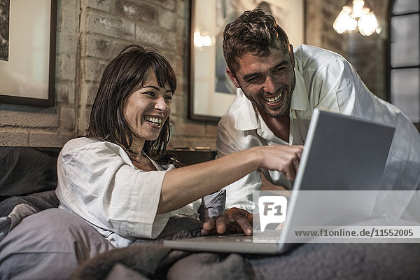 Happy couple together in bed looking at laptop
