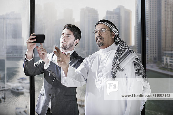 Westliche und nahöstliche Geschäftsleute diskutieren über die Zukunft und halten ein Smartphone in der Hand.