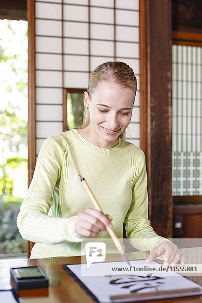 Kaukasische Frau übt Kalligraphie in einem traditionellen japanischen Haus