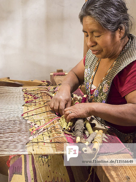 Zapotec woman weaving a rug on a floor loom in farmhouse Teotitlan del Valle Oaxaca Mexico North America
