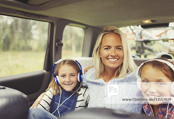 Portrait smiling mother and daughters wearing headphones in back seat of car