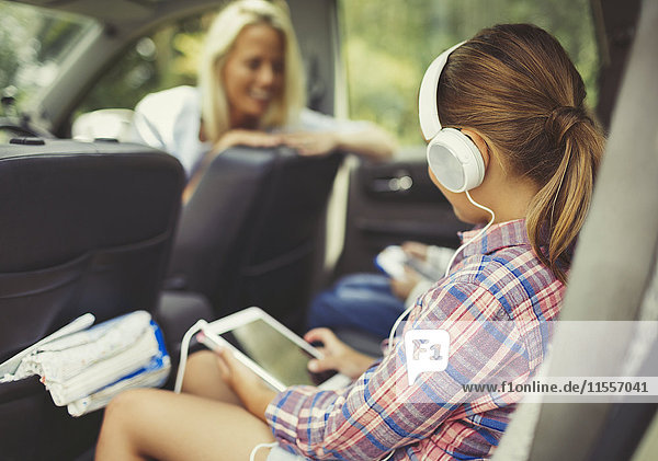 Girl with headphones using digital tablet watching video in back seat of car