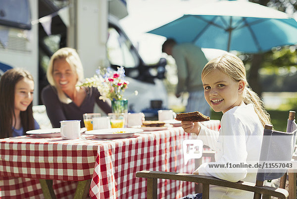 Portrait lächelndes Mädchen beim Frühstücken mit der Familie vor dem sonnigen Wohnmobil