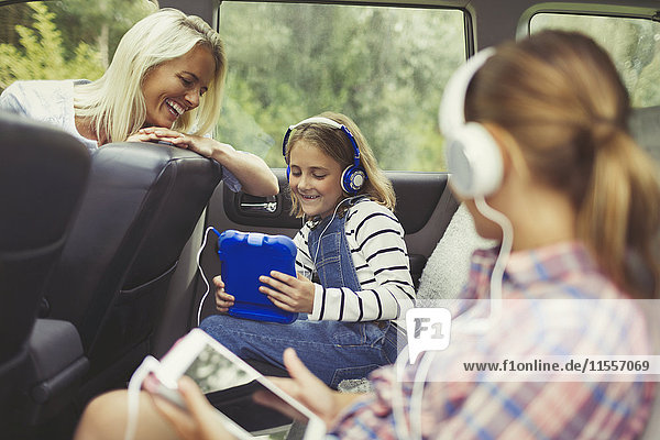 Mutter beobachtet Töchter mit Kopfhörern und digitalen Tabletts auf dem Rücksitz des Autos