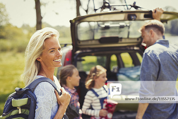 Smiling woman with backpack preparing for hike with family outside car