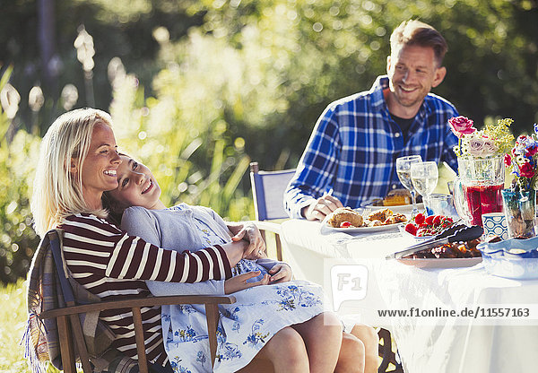 Lächelnde  liebevolle Familie genießt das Mittagessen am sonnigen Gartenparty-Terrassentisch