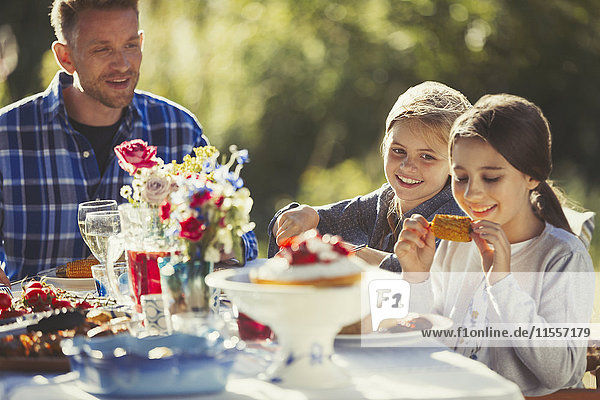 Father watching daughters eating at sunny garden party patio table