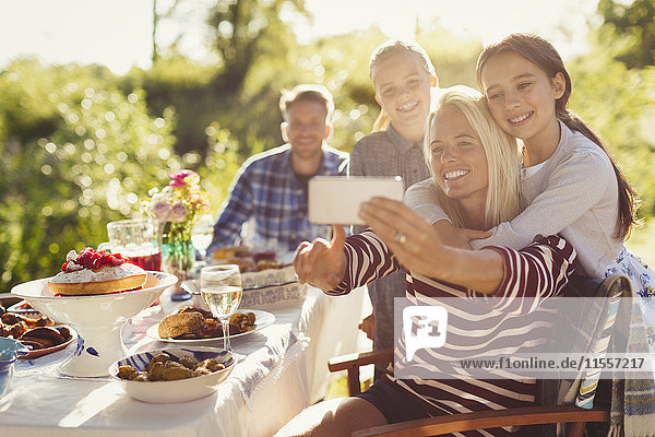 Mother and daughters taking selfie with camera phone at garden party patio table